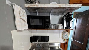 A compact kitchenette with a sink, stove, and microwave. - Bright Seaside Cottage with Panoramic Views in North Truro, Massachusetts (North Truro)