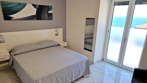 A bedroom with a bed, a nightstand, a wall-mounted artwork, a sliding glass door, and a view of the sea. - At 211 Rooms Guest House - Room No. 1 (Pizzo)