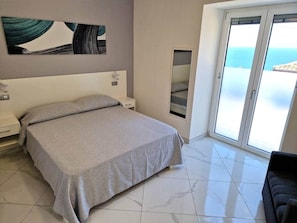Un dormitorio con cama, mesita de noche, una obra de arte en la pared, puerta corrediza de vidrio y vista al mar.
