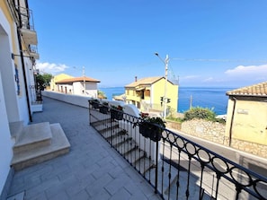 Una calle residencial con vista despejada al mar, un paseo pavimentado y una barandilla de metal.