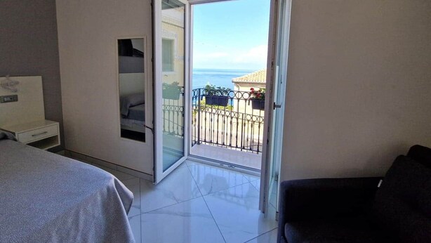 A hotel room with a bed, a desk, a chair, and a balcony with a view of the sea. - At 211 Rooms Guest House - Room No. 1 (Pizzo)