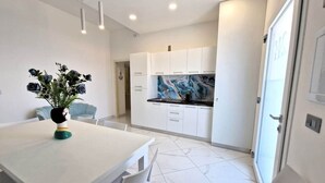 A modern kitchen with white cabinets, a marble countertop, and a dining area with a white table and chairs. - At 211 Rooms Guest House (Room No. 5) (Pizzo)