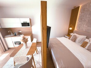 A modern hotel room with a bed, a desk with a chair, a small kitchenette, and a TV mounted on the wall. - Exclusive apartment in the center of Tihany with a two-person hot tub. (Tihany)