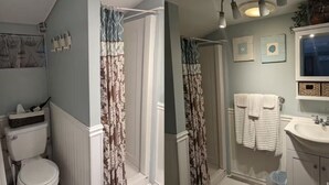 A bathroom with a toilet, shower curtain, sink, and towel rack. - Stone Cottage on Oneida Lake (Brewerton)