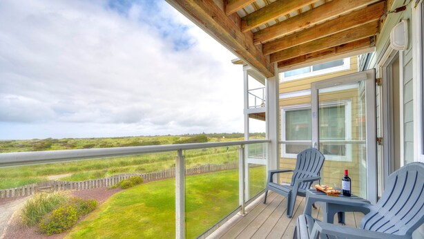 A covered outdoor area with a table and chairs, a bottle of wine, and a view of the landscape. - Ocean & Jetty Views | Pool & Hot tub | #920 (Westport)