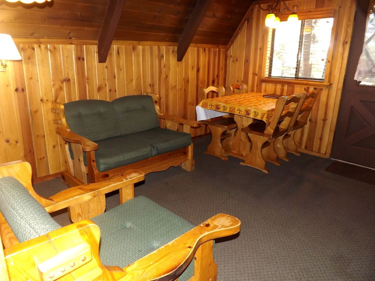 A wooden cabin interior with a sofa, chairs, a table, and a window.