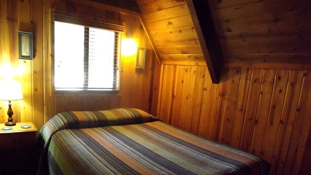 Una habitación de madera con una cama, una ventana y una mesita de noche.