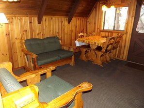 Ein Holzblockhaus-Innenraum mit einer Couch, Sesseln, einem Tisch und einem Fenster.