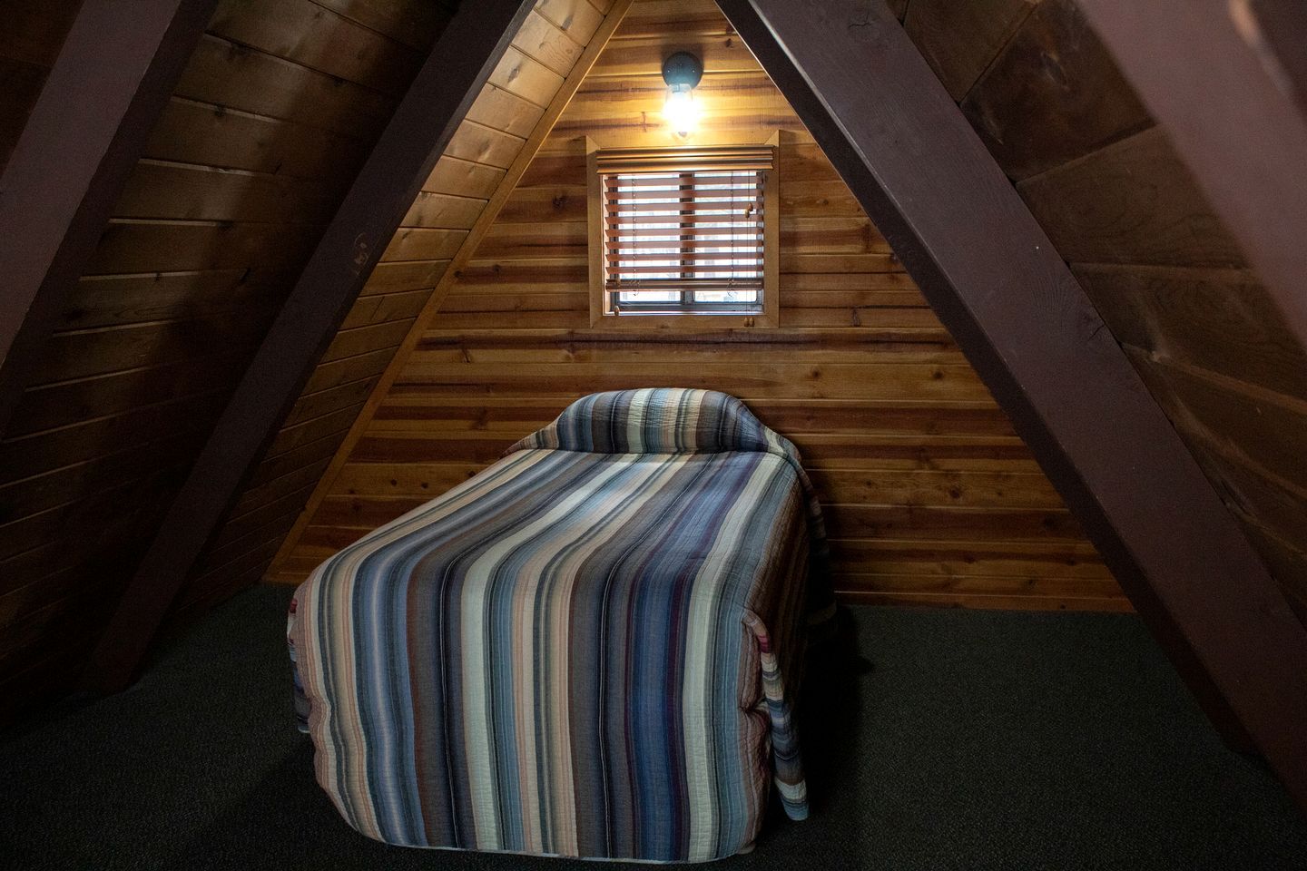 Una cama individual en habitación con paredes de madera inclinadas y un ventanal pequeño.