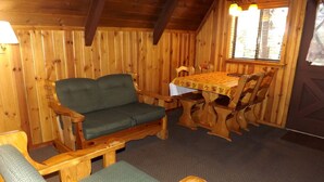 Interior de una cabaña de madera con un sofá, sillas, una mesa y un ventanal.
