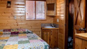 Habitación de cabaña de madera con una cama, un lavamanos pequeño y una ventana con persianas.