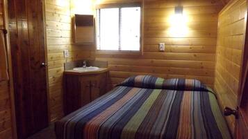 Une pièce dans une cabane en bois, avec un lit, un petit lavabo et une fenêtre.