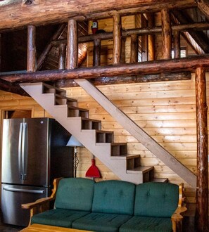 A wooden interior with a staircase, a green sofa, and a stainless steel refrigerator. - Cabin #13 (Flagstaff)