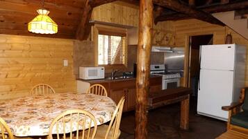 L’intérieur d’un chalet en bois comprend une table à manger, des chaises, un coin cuisine équipé d’appareils électroménagers et un escalier.