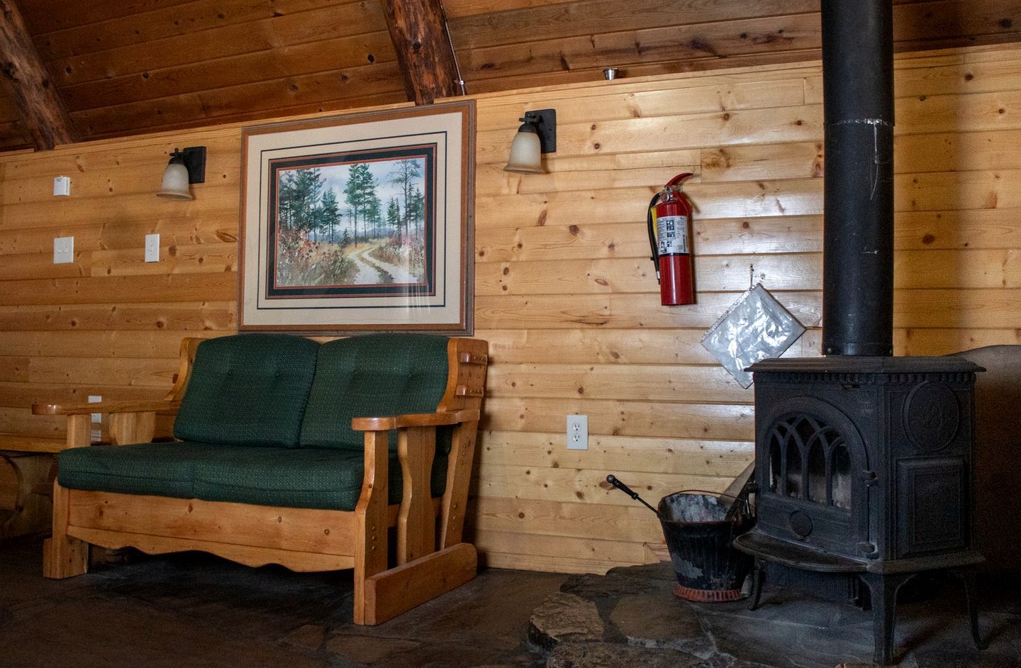Interior acogedor de una cabaña con sofá de madera, chimenea, un cuadro en la pared y un extintor.