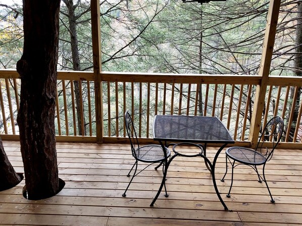 A wooden deck with a table and chairs, surrounded by a railing with a view of trees.