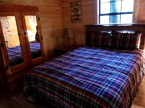 Una habitación de madera con cama, espejo y ventana.