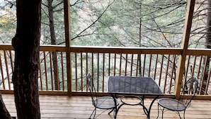 Una terraza de madera con una mesa y sillas, rodeada por una barandilla y vista a árboles.
