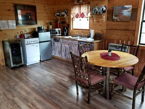 A wooden cabin interior with a kitchen, dining area, and a window with curtains.