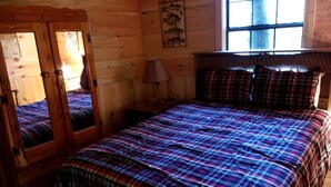Una habitación de madera con cama, espejo y ventana.