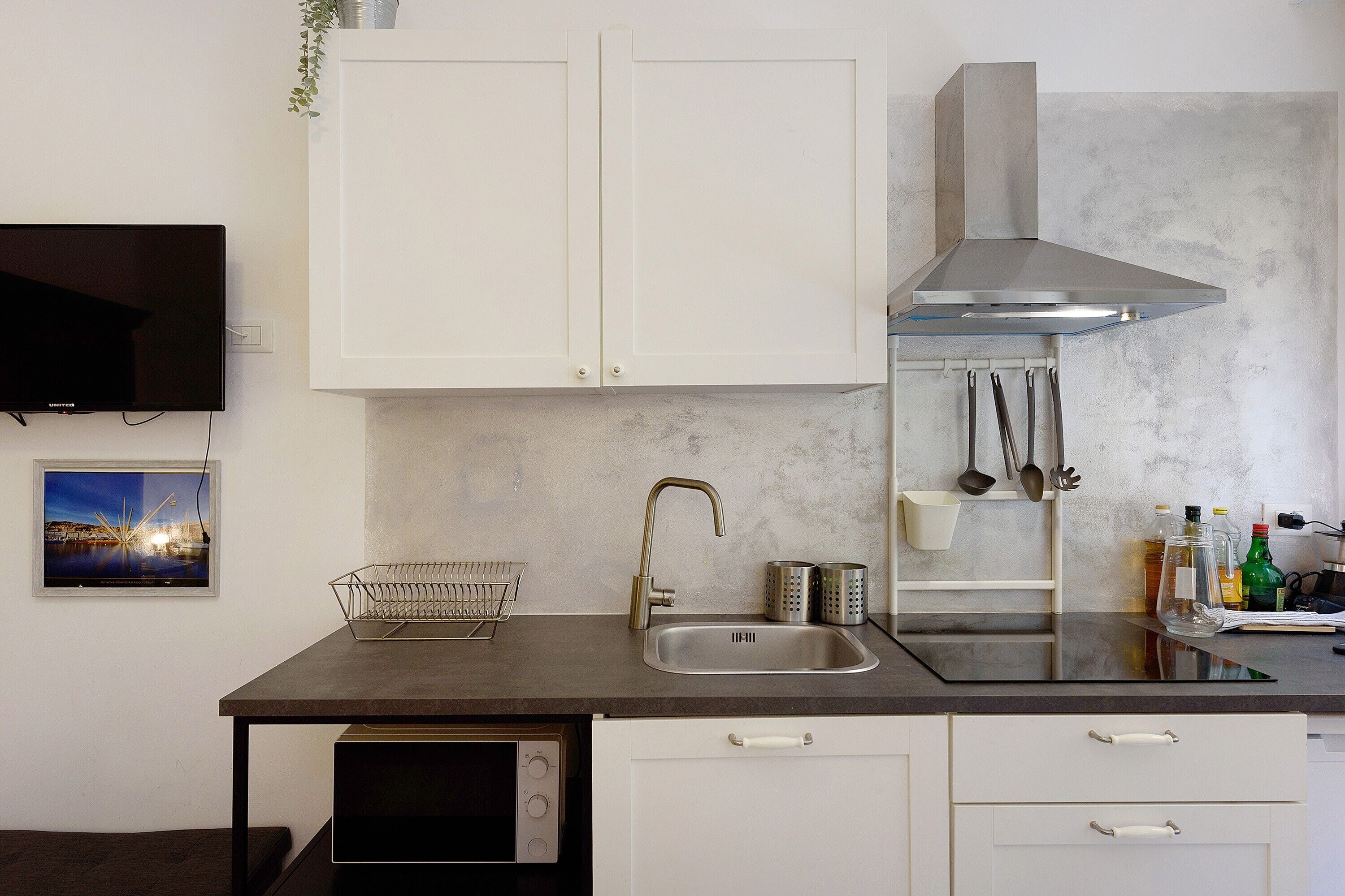 Cocina compacta con armarios blancos, un lavamanos de acero inoxidable y un microondas integrado.