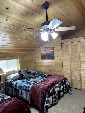 Dormitorio de cabaña de madera con cama, ventilador de techo, ventana y armario.
