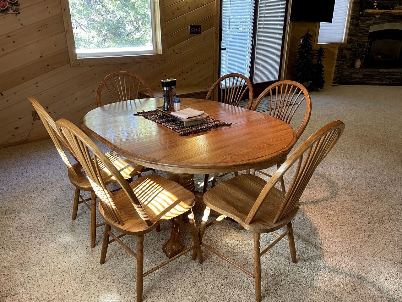 A round wooden dining table with six chairs, a coffee maker, and a placemat.