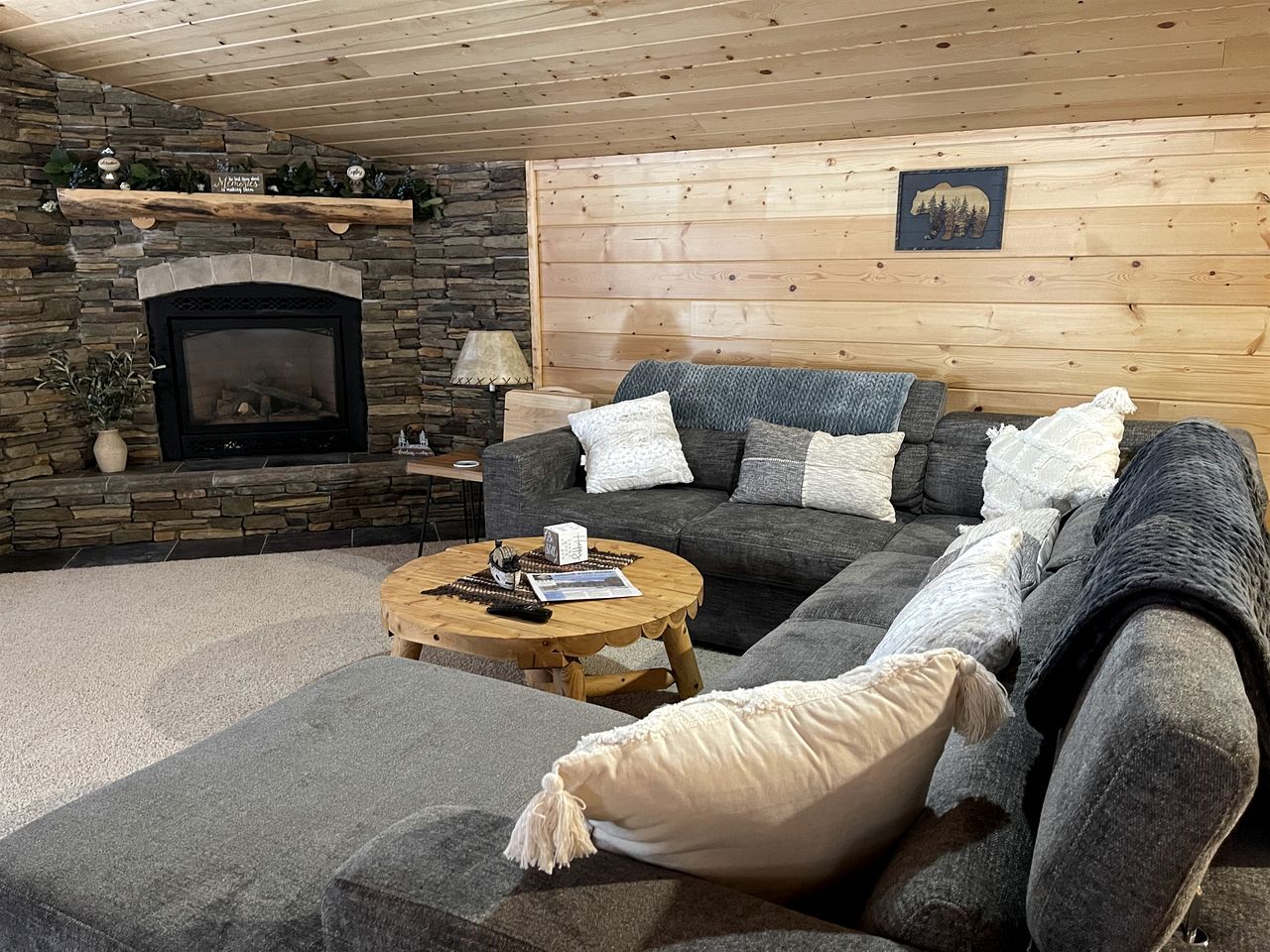 A cozy living room with a stone fireplace, a sofa, a coffee table, and a wooden ceiling.