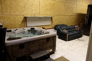 Una habitación con una bañera de hidromasaje de piedra, un sofá de color oscuro y un banco de madera.