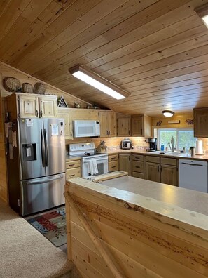 Interior de una cabaña de madera con cocina, que incluye refrigerador, microondas, estufa y armarios de madera.