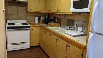 A kitchen with wooden cabinets, a white stove, a microwave, and a refrigerator.