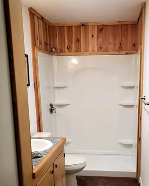 Un baño con tocador de madera, un lavamanos blanco y cabina de ducha.