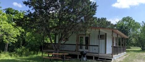 Eine kleine Holzhütte mit Veranda, umgeben von Bäumen und einer Rasenfläche.