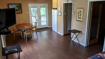 A room with a ceiling fan, a television, a dining table with chairs, a small table, and a door leading to another room.