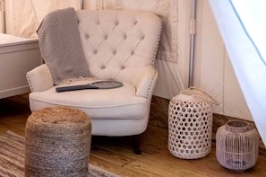 A tufted armchair with a remote control, a woven ottoman, and two wicker lamps.