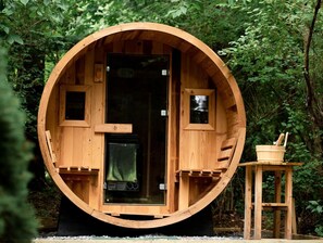 Een houten, cilindervormig gebouw met een deur, ramen en een klein houten krukje met een emmer.