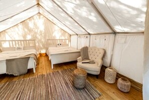 Een tentaccomodatie met een bed, een stoel, een klein tafeltje en een vloerkleed.