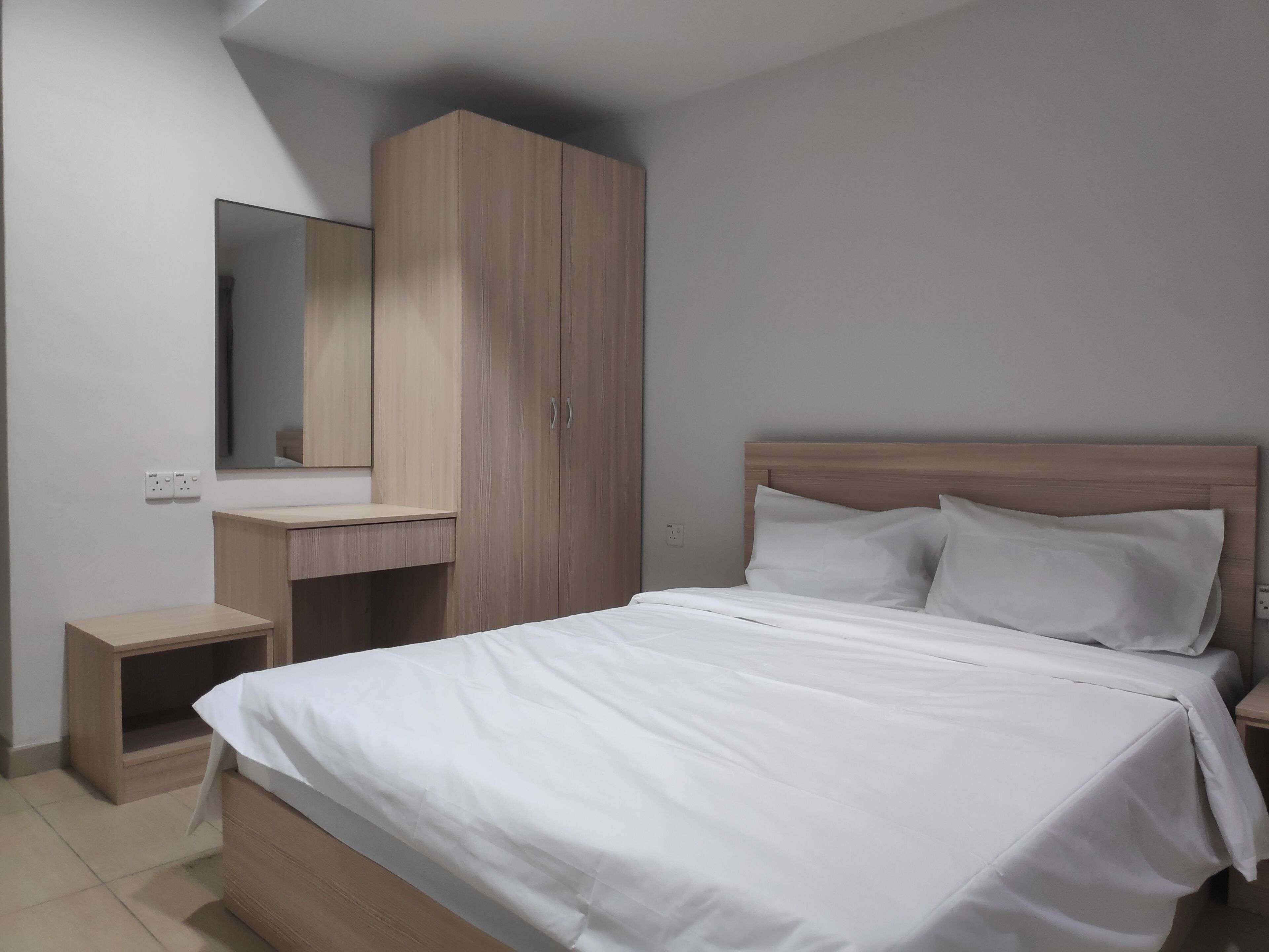 Een slaapkamer met een bed, nachtkastje, dressoir, spiegel en een stopcontact.