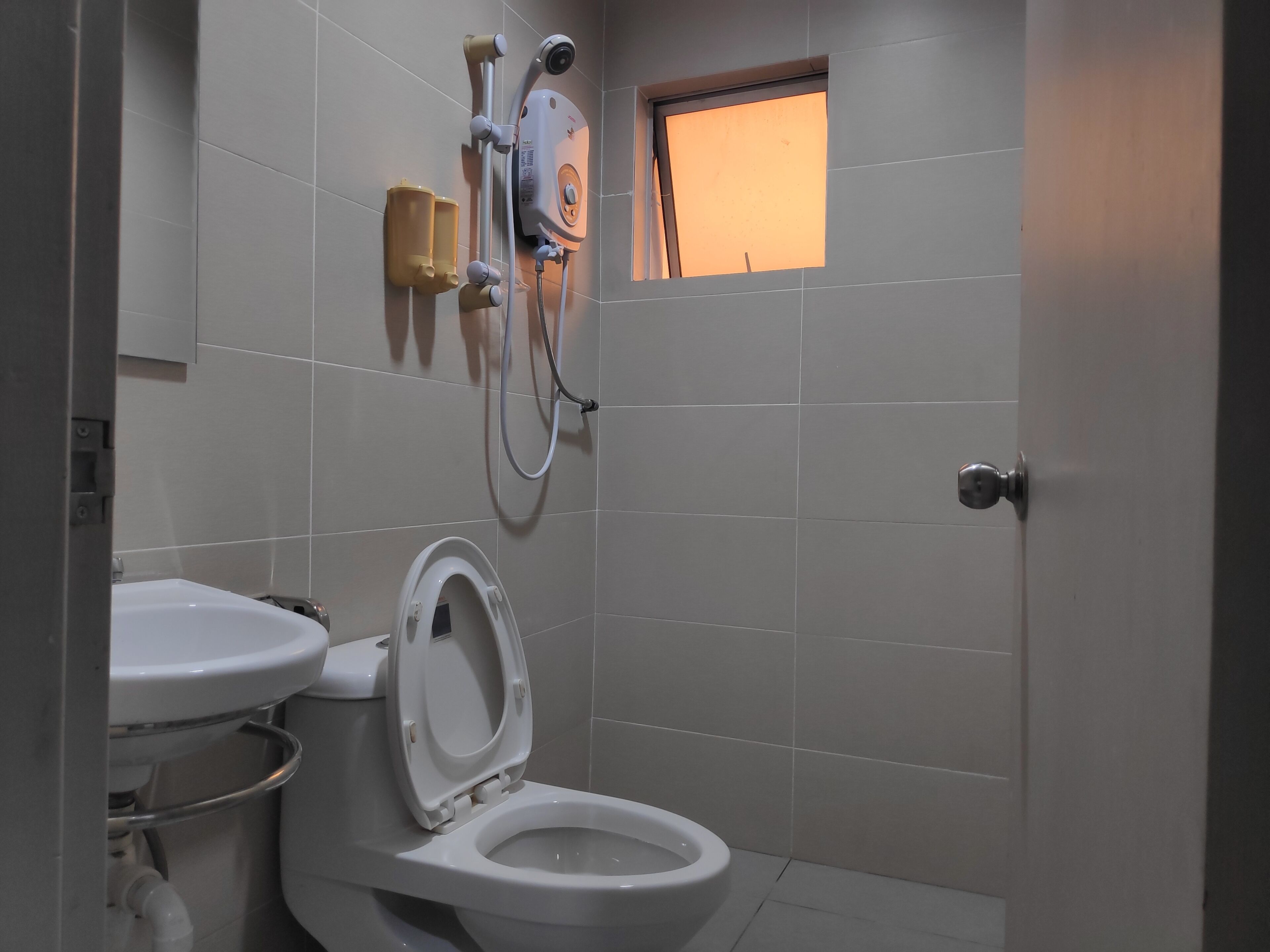 A bathroom with a toilet, a shower unit, and a small window.