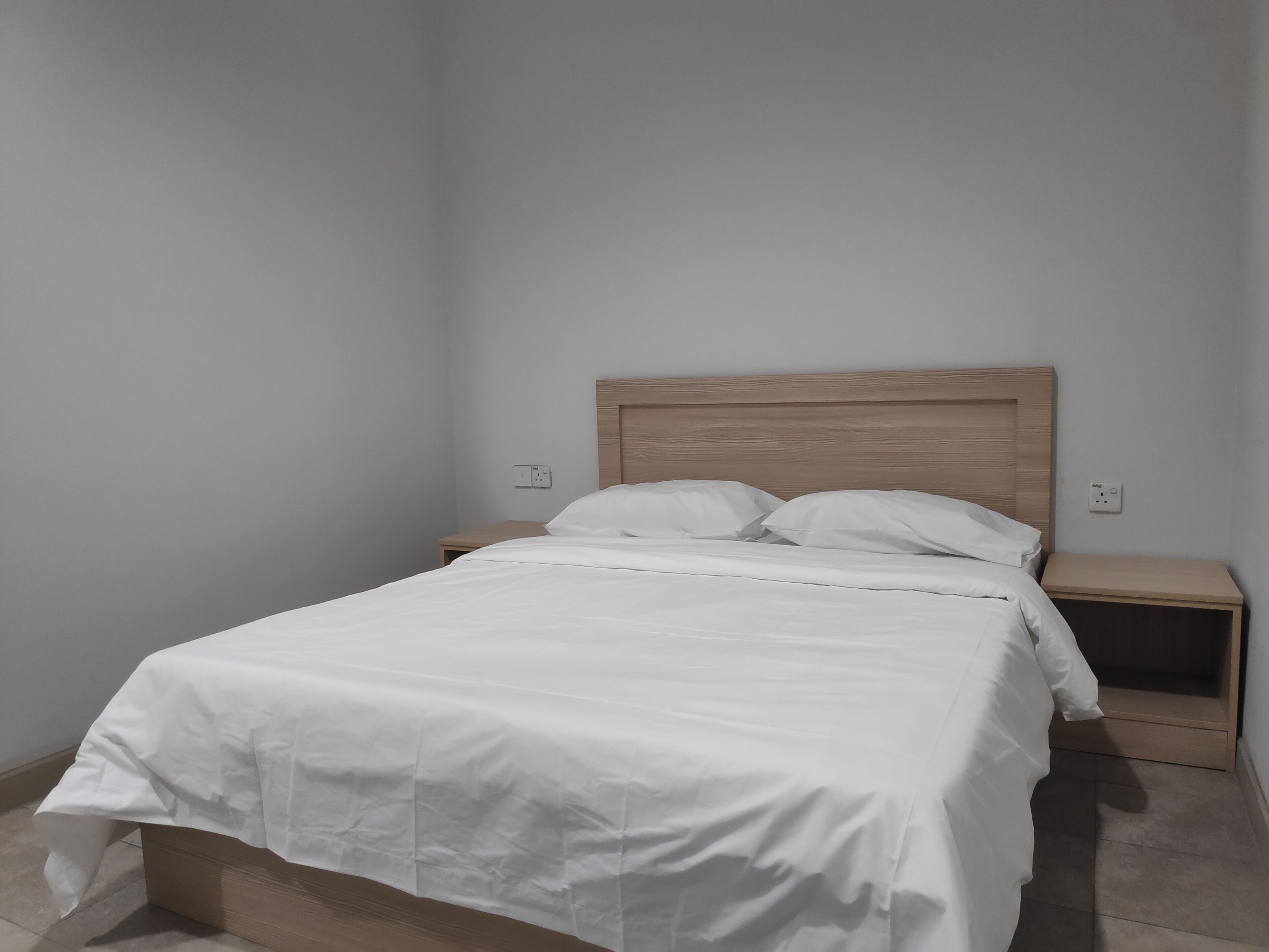 Een enkel bed met een houten hoofdbord, twee nachtkastjes en een effen muur.
