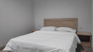 Een enkel bed met een houten hoofdbord, twee nachtkastjes en een effen muur.