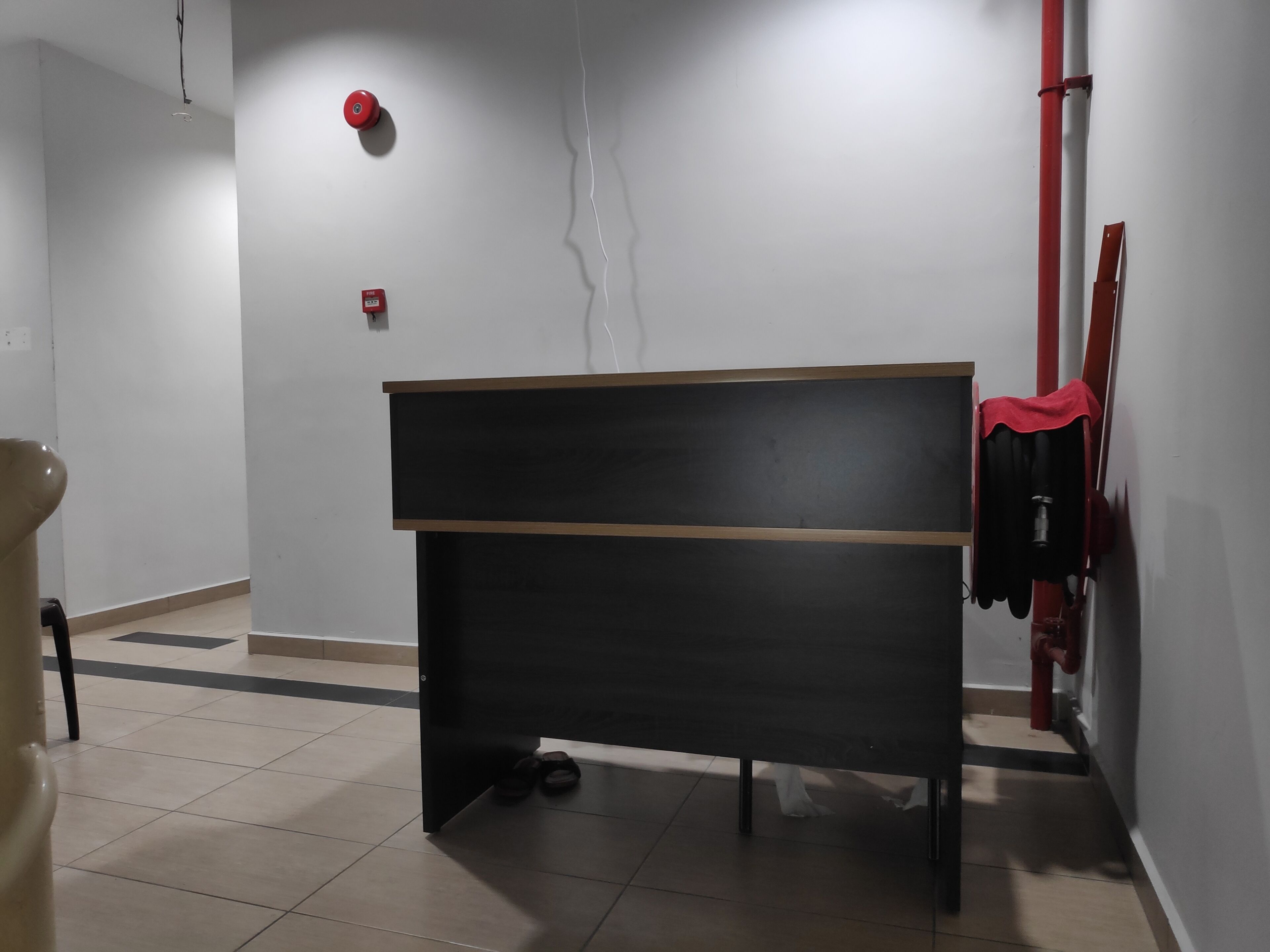 Ein Zimmer mit einem schwarzen Schreibtisch, einem roten Rauchmelder und einem roten Feuerwehrschlauch an der Wand.