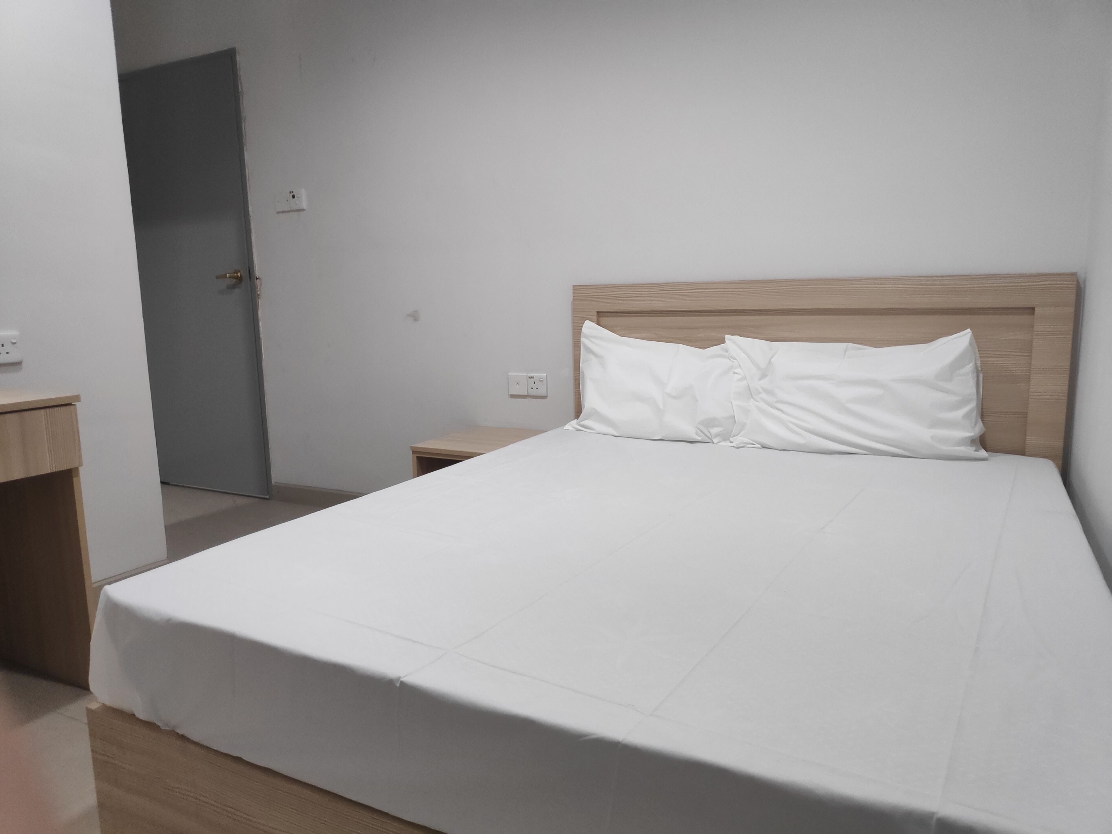 A hotel room with a large bed, a wooden headboard, a nightstand, and a door leading to another room.