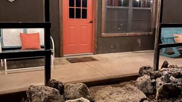 A building with a red door, a bench with an orange cushion, and a stone pathway leading to the entrance.