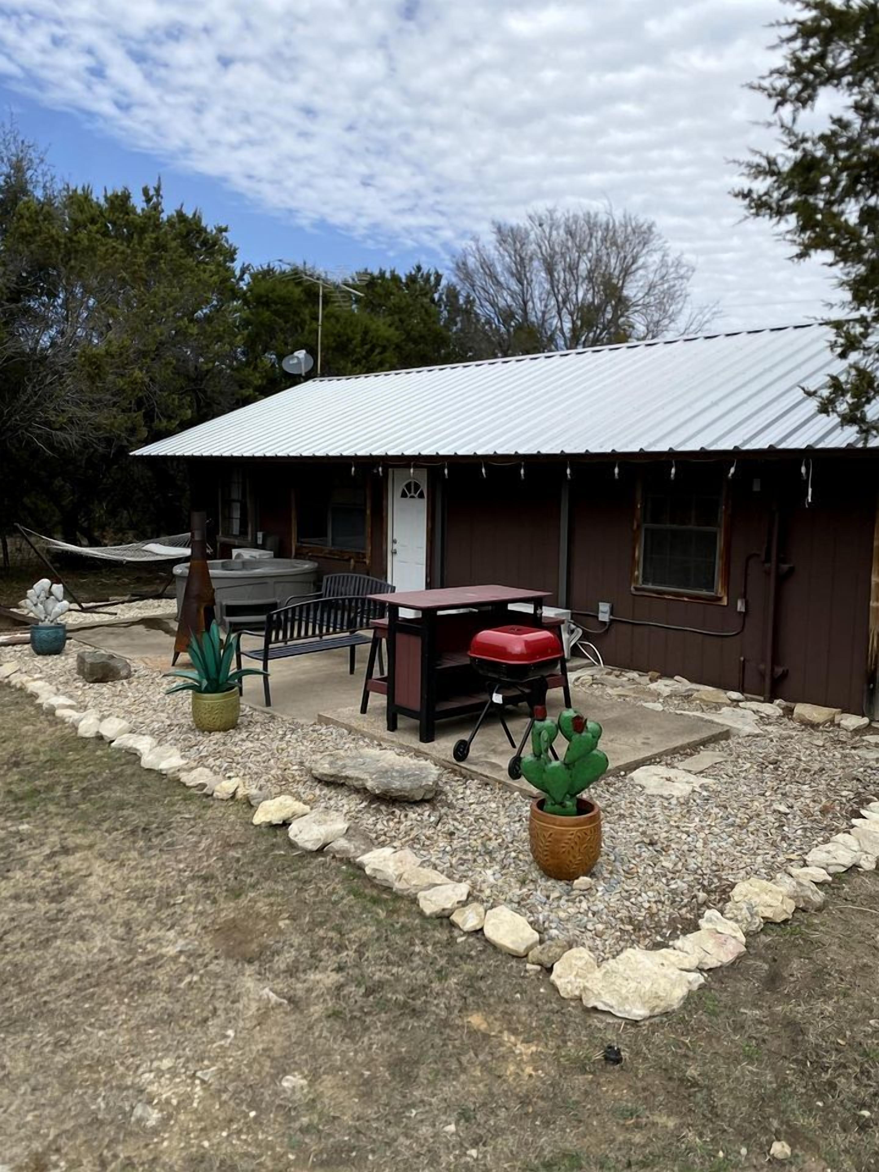 A rustic cabin with a metal roof, outdoor seating, and a barbecue grill.