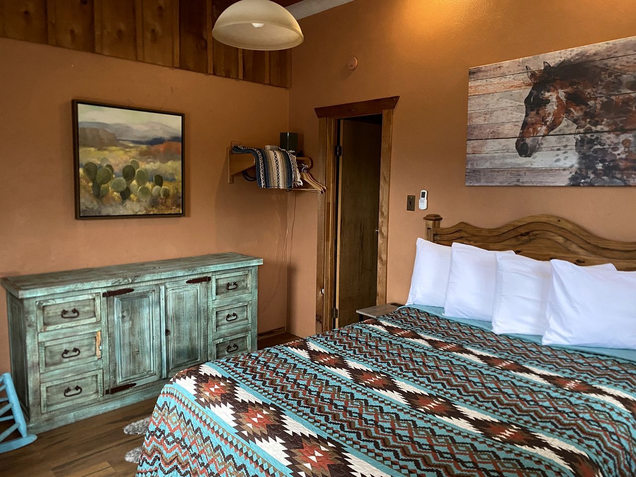 A bedroom with a bed, a dresser, a door, and a wall painting.