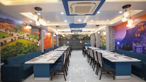 A restaurant with long tables, blue cushioned seating, and murals on the walls. - Hotel Pearl Heritage (Jaipur)