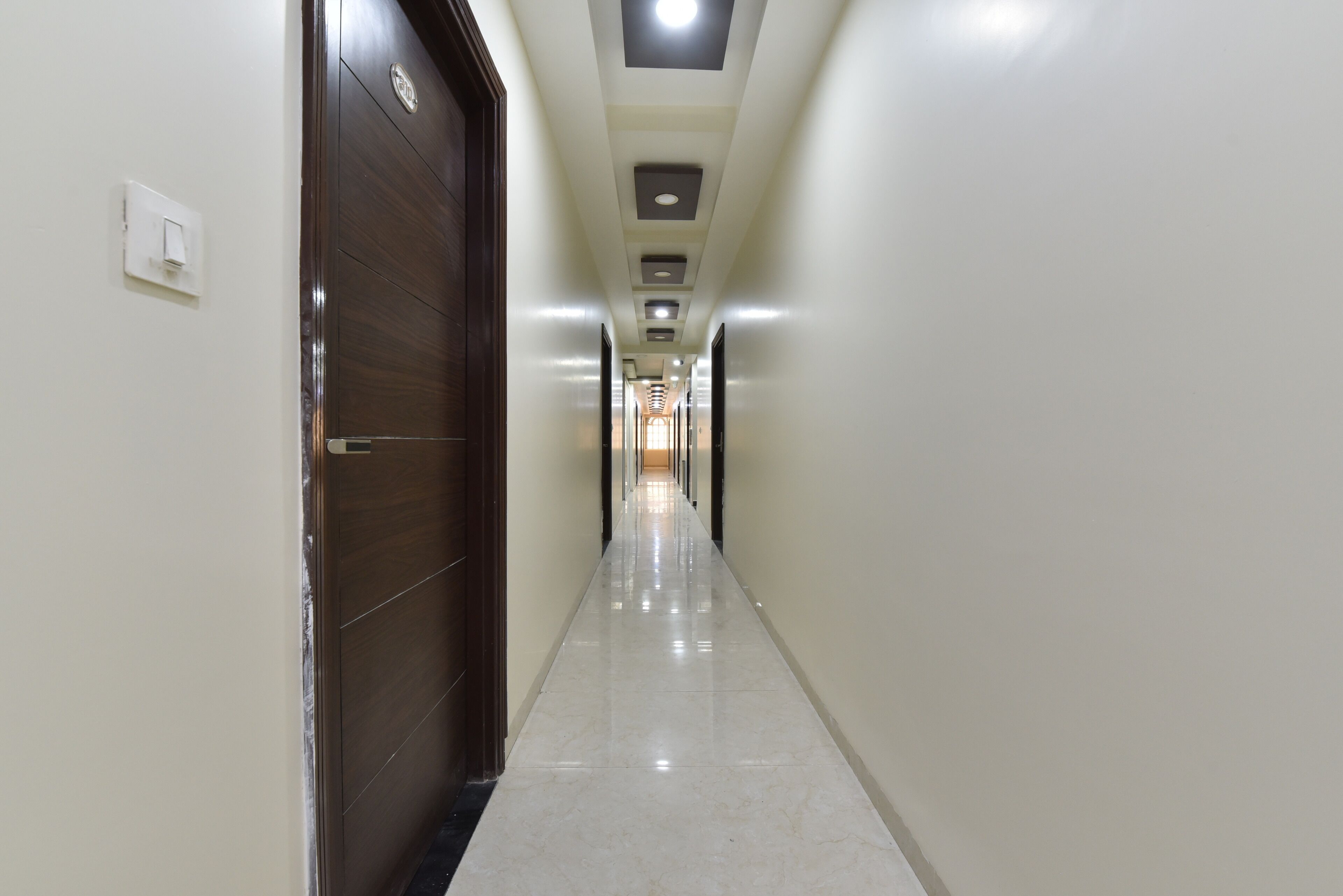 A long, narrow hallway with a wooden door on the left and a light switch on the wall.