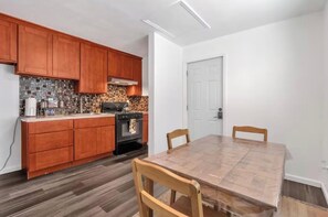 Una cocina con armarios de madera, salpicadero de azulejos, estufa y una mesa de comedor con sillas.