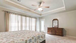A bedroom with a bed, a dresser, a ceiling fan, and a door.